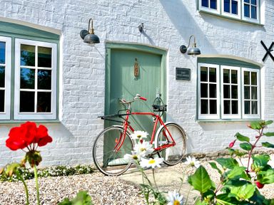 A red bicycle leaning against a green door on a white brick building with wall lights and flowers in the foreground at Old Post Office in Sherborne