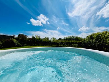 An outdoor hot tub with water bubbles surrounded by green bushes and trees under a blue sky at Old Post Office in Sherborne
