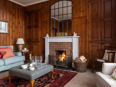 A living room with a fireplace wood-paneled walls sofas a coffee table and a basket of firewood at Flagstaff in Penmon near Beaumaris