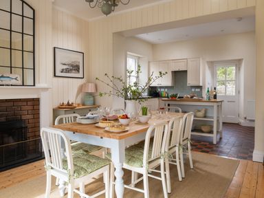 A dining area with a wooden table and chairs with cushions next to a kitchen with white cabinets at Flagstaff in Penmon near Beaumaris