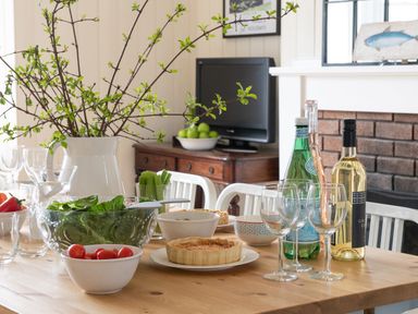 A dining table with salad bowls wine bottles glasses and a vase in a dining room at Flagstaff in Penmon near Beaumaris