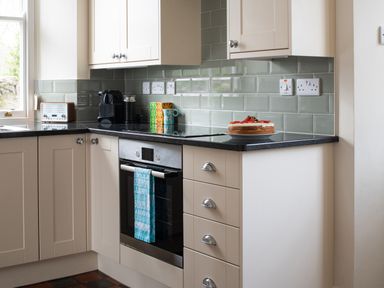 A kitchen corner with white cabinets a black countertop an oven a coffee machine and a cake on the counter at Flagstaff in Penmon near Beaumaris