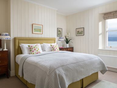 A bedroom with a bed with patterned pillows bedside tables lamps and framed pictures on the wall at Flagstaff in Penmon near Beaumaris