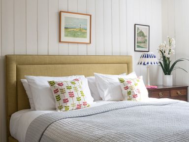 A bed with patterned pillows and a gray blanket next to a wooden nightstand with a lamp and flowers at Flagstaff Penmon near Beaumaris