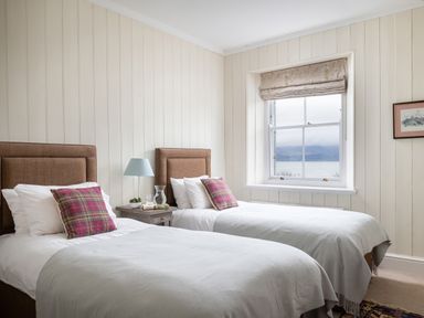 A bedroom with two single beds side by side with plaid cushions and a window with a view at Flagstaff Penmon near Beaumaris