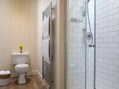 A bathroom with a toilet, towel rack with towels, shower area with glass door and white tiled walls at Flagstaff in Penmon near Beaumaris