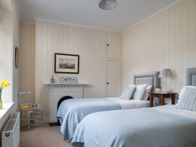 A bedroom with two single beds a bedside table a chair a fireplace and wall art at Flagstaff in Penmon near Beaumaris