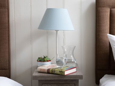 A bedside table with a blue lampshade, a book, a glass and a jug of water, and a bowl of strawberries at Flagstaff in Penmon near Beaumaris