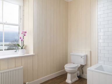 A bathroom with a toilet and a bathtub next to a window with an orchid on the windowsill at Flagstaff in Penmon near Beaumaris