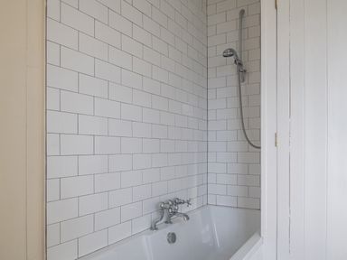 A bathroom with a white bathtub chrome taps and a showerhead on white tiled walls at Flagstaff in Penmon near Beaumaris