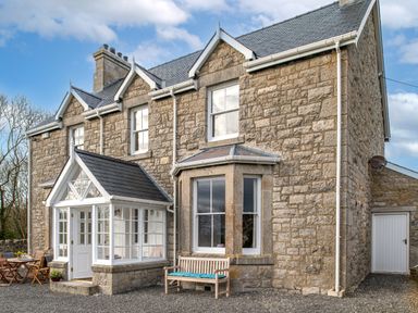 Stone house with white window frames a wooden bench and outdoor table with chairs at Flagstaff in Penmon near Beaumaris