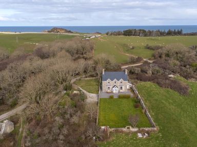 A stone house with a fenced garden surrounded by fields and trees with the sea in the background at Flagstaff Penmon near Beaumaris