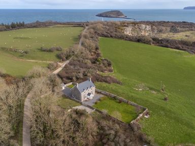 A stone house with a lawn and surrounding fields overlooking the sea and an island at Flagstaff Penmon near Beaumaris