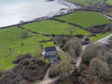 A countryside house with fenced garden near green fields and a coastline at Flagstaff in Penmon near Beaumaris