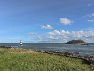 A coastal scene with a lighthouse in the sea and an island in the distance at Flagstaff Penmon near Beaumaris
