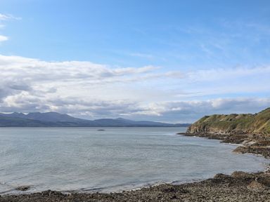 A coastline with rocky shore and hills in the distance at Flagstaff in Penmon near Beaumaris
