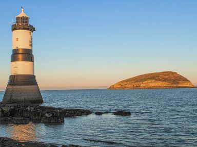 A lighthouse on rocky shore with an island in the sea at Flagstaff in Penmon near Beaumaris