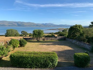 A garden with trimmed hedges and trees overlooking a bay and mountains at Flagstaff Penmon near Beaumaris