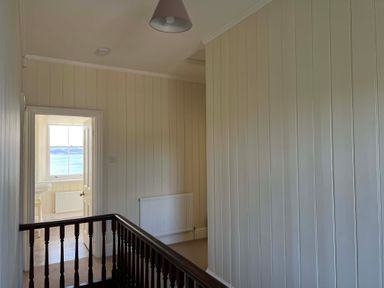A hallway with vertical panel walls a wooden railing and a door leading to a room with a window showing a sea view at Flagstaff in Penmon near Beaumaris