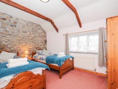 A bedroom with two wooden beds blue blankets stone wall and window with curtains at Mum's Cottage in Minions near Upton Cross