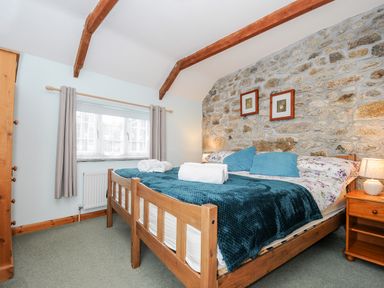 A bedroom with a wooden bed a stone wall and wooden furniture at Mums Cottage Minions near Upton Cross