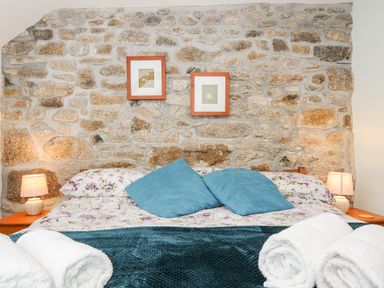 A bed with floral sheets blue pillows and rolled white towels against a stone wall with two framed pictures at Mum's Cottage in Minions near Upton Cross