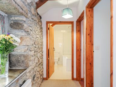 A hallway with stone wall and wooden door frames leading to a bathroom with a toilet and bathtub at Mum's Cottage Minions near Upton Cross