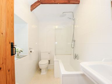 A bathroom with a wooden door a toilet a bathtub with shower and a sink at Mums Cottage in Minions near Upton Cross