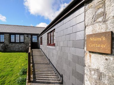 Exterior view of a stone cottage with a ramp leading to a dark door and a sign saying Mum's Cottage in Minions near Upton Cross