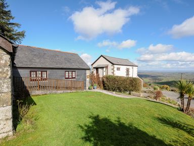 Two cottages with a grassy lawn and a distant rural landscape at Mums Cottage in Minions near Upton Cross