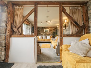 A living room with yellow and grey sofas stone walls and wooden beams at Mums Cottage Minions near Upton Cross
