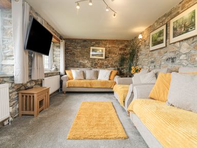 A living room with stone walls two sofas with yellow cushions and a yellow rug at Mum's Cottage Minions near Upton Cross