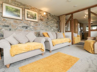 A living room with stone wall two framed pictures two gray sofas with yellow throws and pillows and wooden beams at Mums Cottage Minions near Upton Cross
