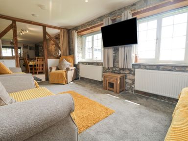 A living room with armchairs a sofa a wall mounted television and a small wooden table at Mums Cottage Minions near Upton Cross