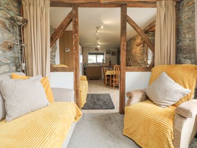A living room with armchairs covered in yellow throws facing a kitchen and dining area at Mums Cottage in Minions near Upton Cross