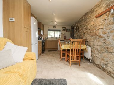 A kitchen and dining area with wooden cabinets a white refrigerator a stone wall and a table with chairs at Mum's Cottage in Minions near Upton Cross