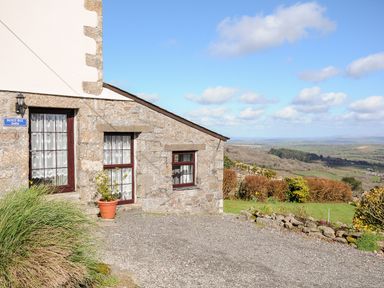 Exterior of a stone barn with windows and a potted plant overlooking a landscape with fields and bushes at Bickle Bice Cottage in Minions near Liskeard