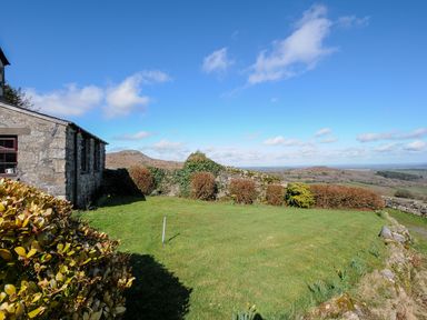 A garden with stone walls bushes and a stone building under a blue sky at Bickle Bice Cottage Minions near Liskeard