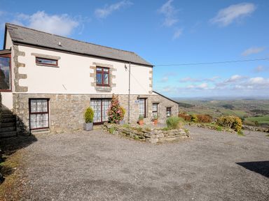 A stone and stucco house with gravel driveway and potted plants overlooking a valley at Bickle Bice Cottage Minions near Liskeard
