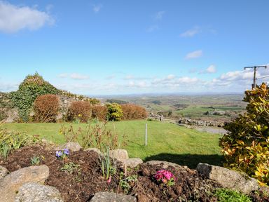 A garden with flower beds and shrubs overlooking a green landscape at Bickle Bice Cottage in Minions near Liskeard
