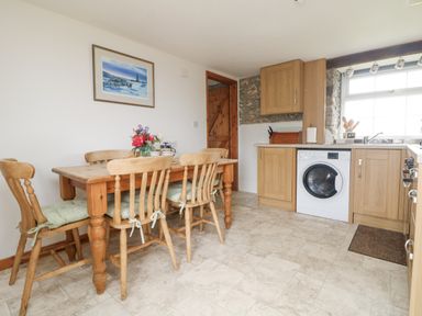 A kitchen with wooden dining table and chairs washing machine and cabinets at Bickle Bice Cottage in Minions near Liskeard