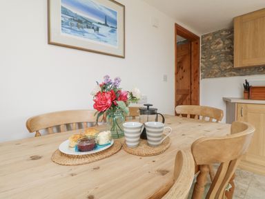 A wooden dining table with flowers scones jam cream cups and a coffee press in a kitchen at Bickle Bice Cottage in Minions near Liskeard