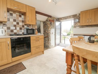 A kitchen with wooden cabinets a dining table and chairs an oven a microwave and a door leading outside at Bickle Bice Cottage Minions near Liskeard