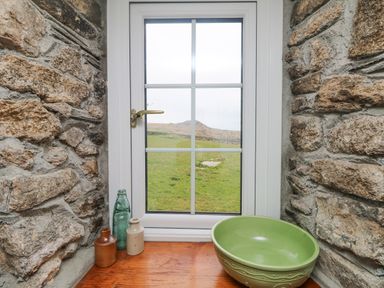 A window with a brass handle set in a stone wall with a green bowl and three small bottles on a wooden sill at Bickle Bice Cottage in Minions near Liskeard
