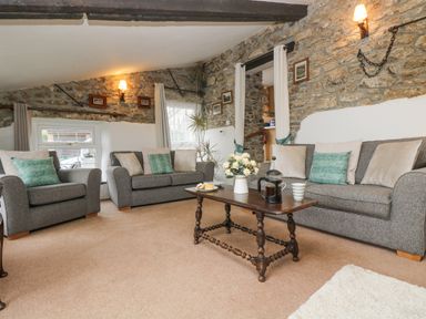 A living room with grey sofas a wooden coffee table and stone walls at Bickle Bice Cottage in Minions near Liskeard