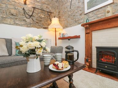 A living room with a stone wall sofa and coffee table with flowers cups scones and a coffee pot by a fireplace at Bickle Bice Cottage in Minions near Liskeard