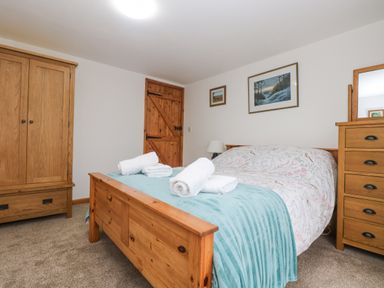 A bedroom with a wooden bed with folded towels a wooden wardrobe and a wooden chest of drawers at Bickle Bice Cottage in Minions near Liskeard