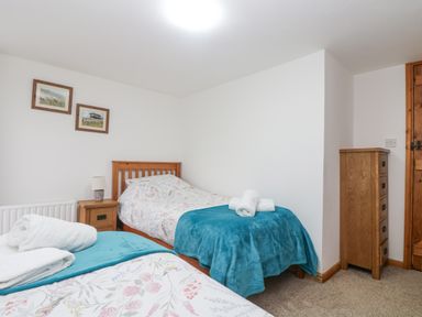 A bedroom with two single beds side by side with blue throws and white towels on top a nightstand with a lamp between the beds two framed pictures on the wall a tall wooden chest of drawers and a wooden door at Bickle Bice Cottage in Minions near Liskeard