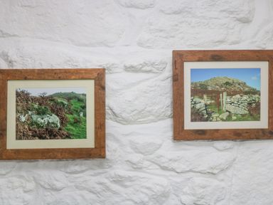 Two framed landscape photographs of rural scenes on a white stone wall at Bickle Bice Cottage in Minions near Liskeard