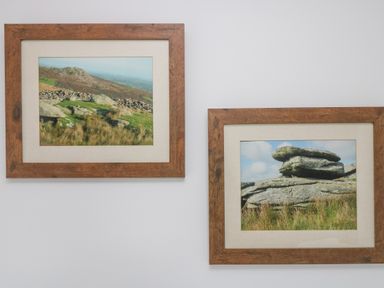 Two framed landscape photographs of rocky hills and grassy fields on a white wall at Bickle Bice Cottage in Minions near Liskeard